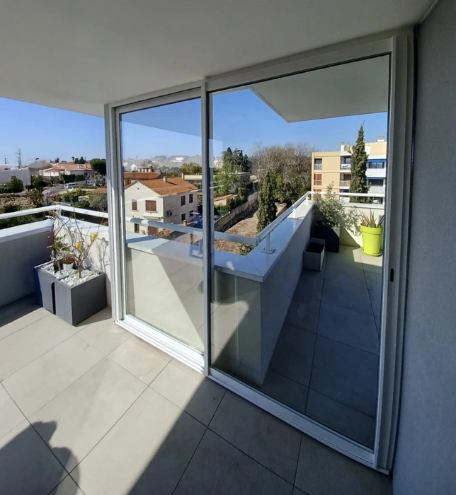 Terrasse moderne d'appartement avec grande baie vitrée coulissante en aluminium donnant sur balcon carrelé