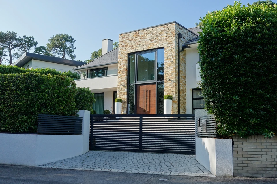 Extérieur résidentiel avec portail coulissant en lames verticales brun foncé intégré dans clôture mixte