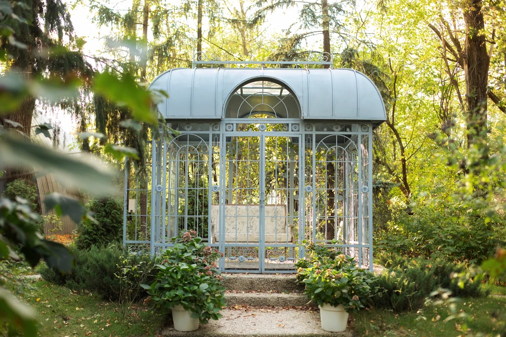Serre de jardin en aluminium et verre installée sur terrasse en bois dans jardin paysagé